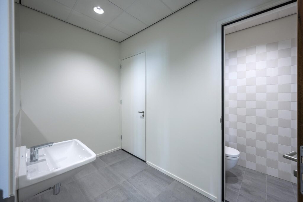 Modern restroom with a wall-mounted sink and a separate toilet area featuring tiled walls.